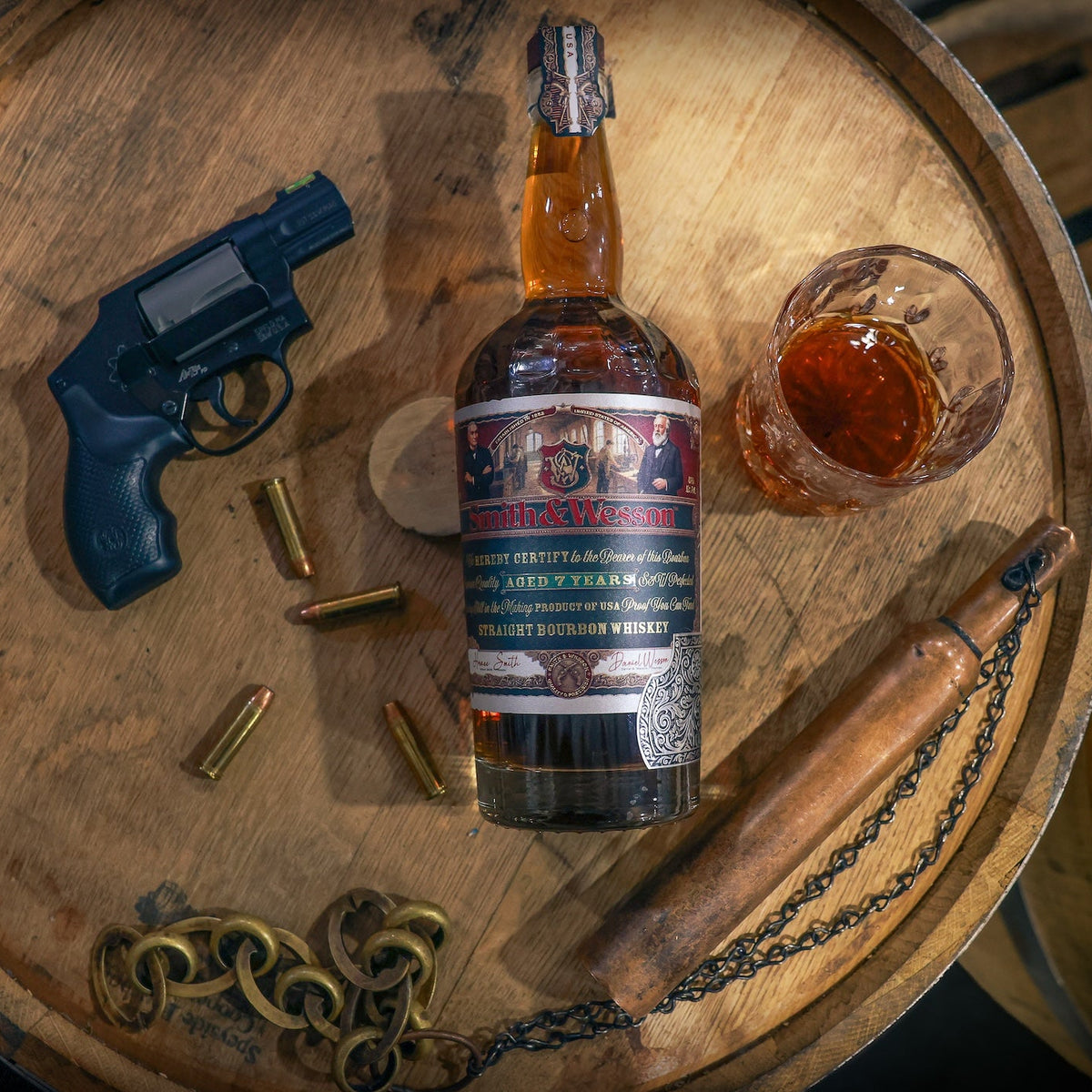 Smith & Wesson™ bottle next to gun, gun shell casings, whiskey glass on top of barrel
